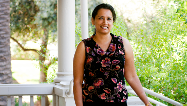Indian female staff member with Help Center, standing on white porch with greenery in background.