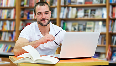 Man studying with laptop and book at library