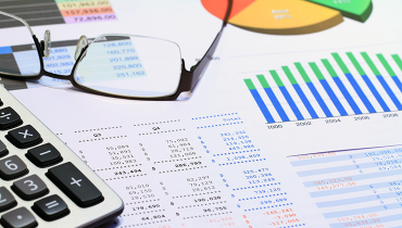 Calculator and reading glasses on financial statement with pie chart, bar graph and figures.