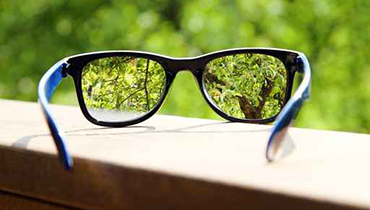 Magnified view of foliage through pair of glasses lying on a wooden surface