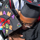 Black undergraduate student hugging classmate whose mortarboard reads "Mama, we made it."