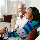 Middle aged female and husband at home while nurse test female's blood pressure