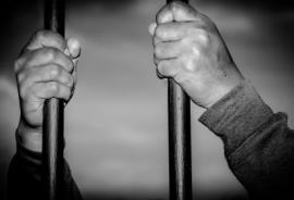 hands gripping jail bars as if from the inside of a jail cell