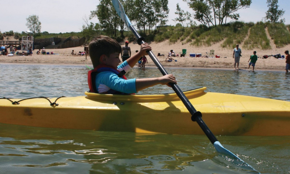 A young child paddles in a kayak near the shore of a beach.