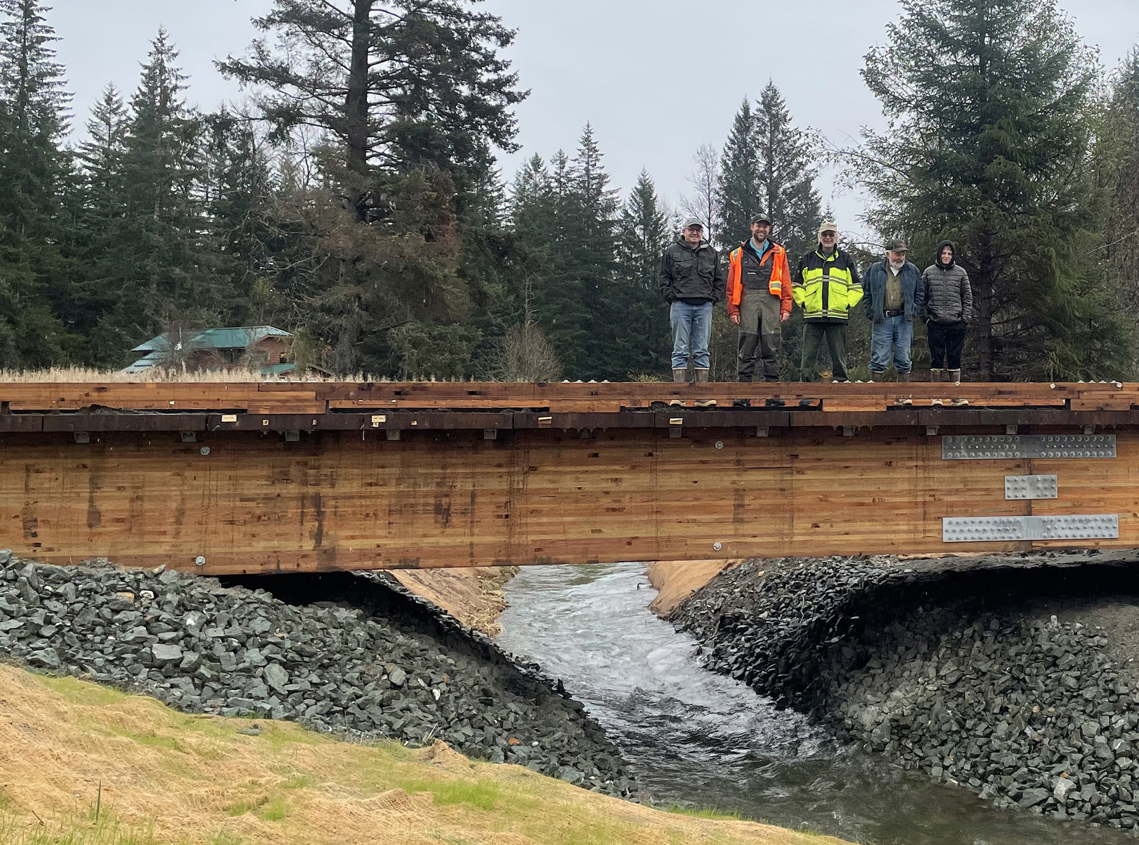 Five people stand on a bridge with a river flowing underneath it and tall trees stand in the background. Photo by Trent Liebich / USFWS 