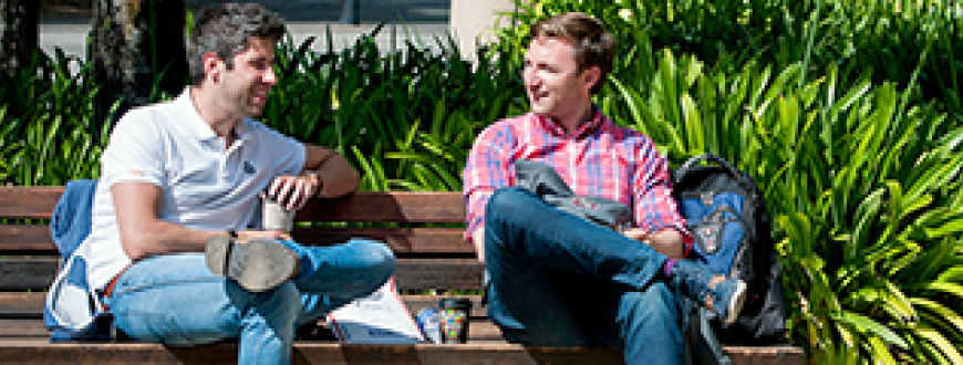Two male students talking while sitting on a sunny bench