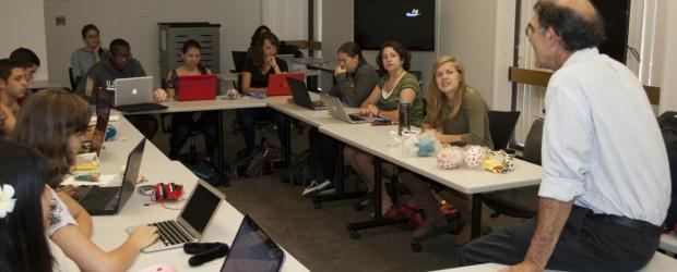 Prof sits on table, students in seminar around tables