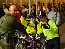 CBP agent with two bicyclists at the U.S.-Mexico border with a large crowd traveling to Juarez, Mexico.