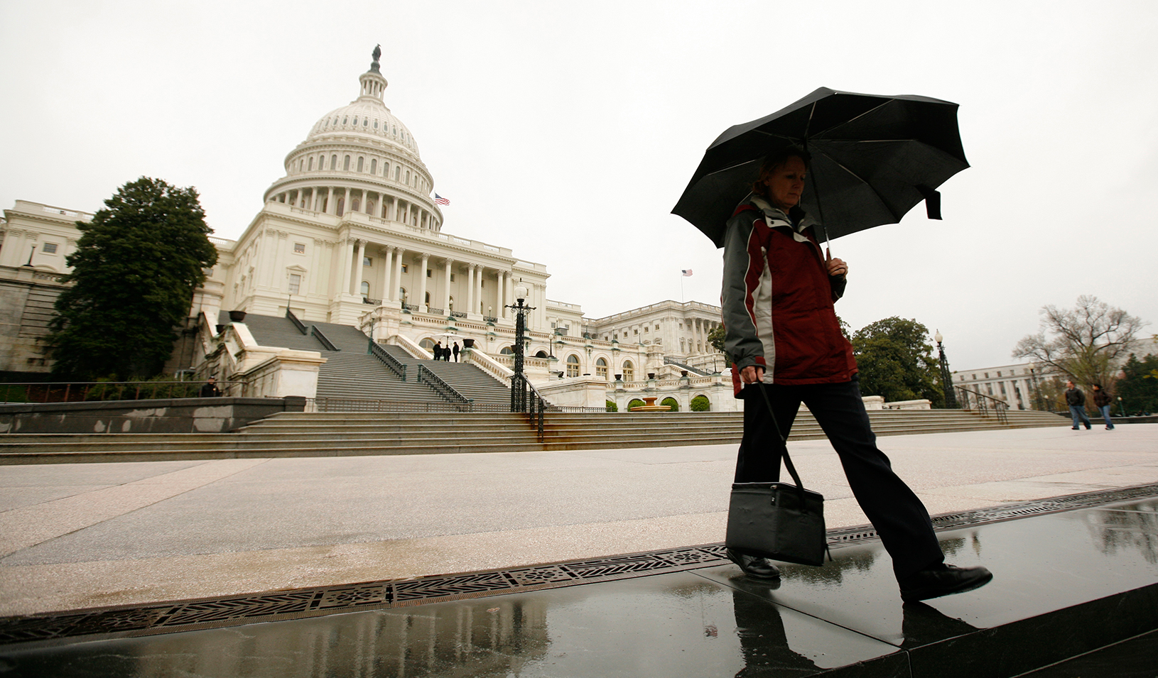 Man with an umbrella walking in front of the Capital