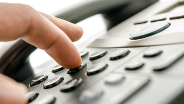 Close up of a hand dialing on an office phone keypad.