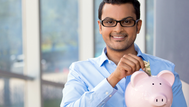 Young man wearing glasses with money in piggy bank