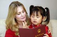 Caucasian mother reading a book with her Chinese daughter on the sofa.