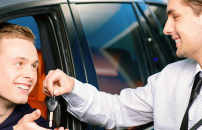 Male rental car representative giving car keys to male customer through driver seat window.