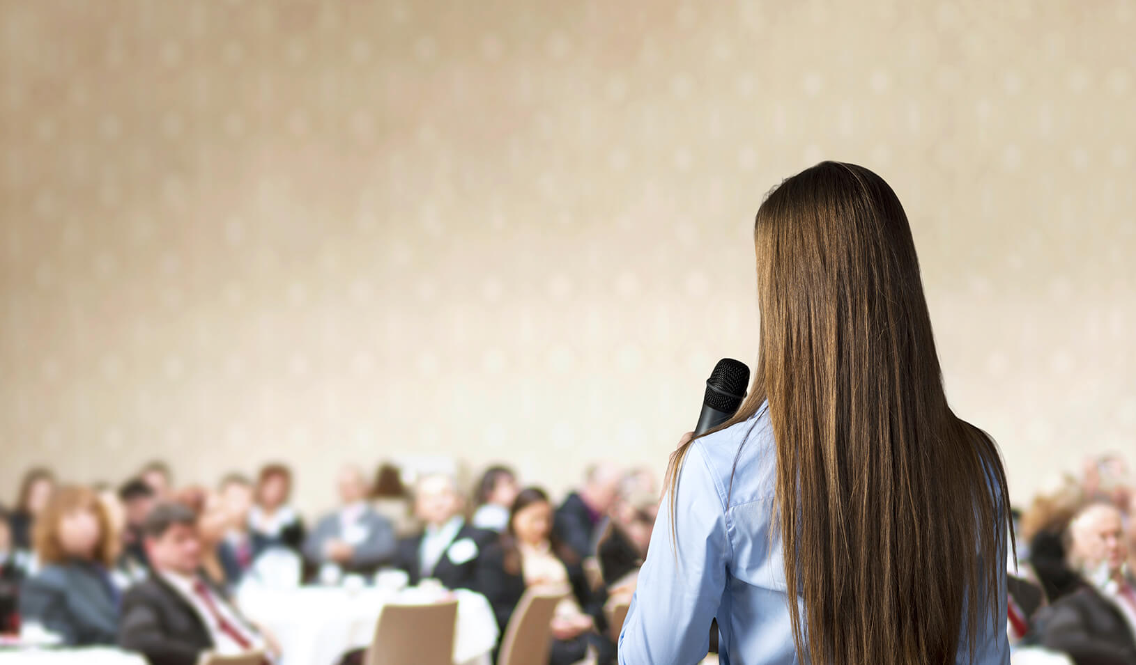Woman speaking in front of a crowd | iStock/Halfpoint