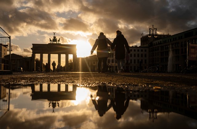 People and the Brandenburg Gate are reflected in a puddle during sunset, in Berlin, Monday, April 5, 2021. (Christophe Gateau/dpa via AP)