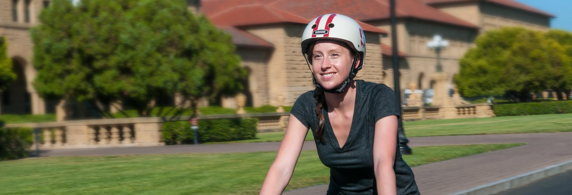 Smiling female cyclist wearing a Stanford-branded helmet riding on Serra Mall.