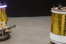 Photo of two of the space robots, which are large cylinders with gold foil around them and a ring of lights at the top.