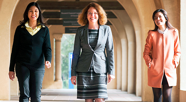 Three female colleagues, one Caucasian, one Eurasian, one Asian, walking through hallway arches