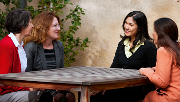 Four female colleagues talking around a wooden table outside