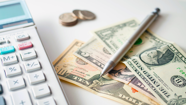 Calculator next to dollar bills, coins and a pen