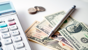 Calcuator next to mechanical pencil, dollar bills and coins