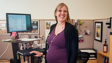 Cheerful pregnant female staffer at computer work station