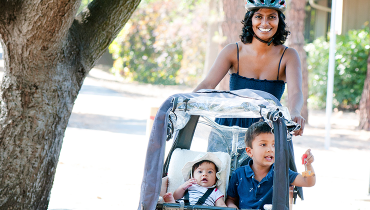 Indian female faculty member pushing baby carriage with her son and daughter inside.