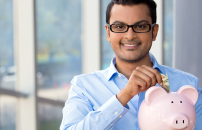 Young Indian male student wearing glasses withdrawing money from piggy bank