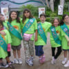 A row of Girl Scouts in green T-shirts and Scout sashes