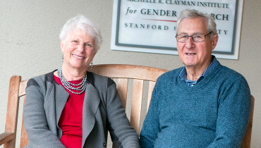 Retired professor emerita and her husband sitting on bench holding hands in front of Clayman Center