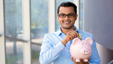Young Indian male putting money in a piggy bank