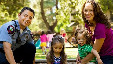 Hispanic male staff member with wife playing with young son and daughter on lawn.