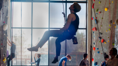 man climbing indoor rock with ropes