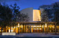 Bing Concert Hall at night, with light glowing through glass walls.