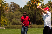 A female and two male youth playing volleyball on Stanford lawn bordered by palm trees.