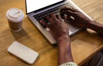 hands typing on a laptop with a coffee cup and cell phone on desk next to laptop