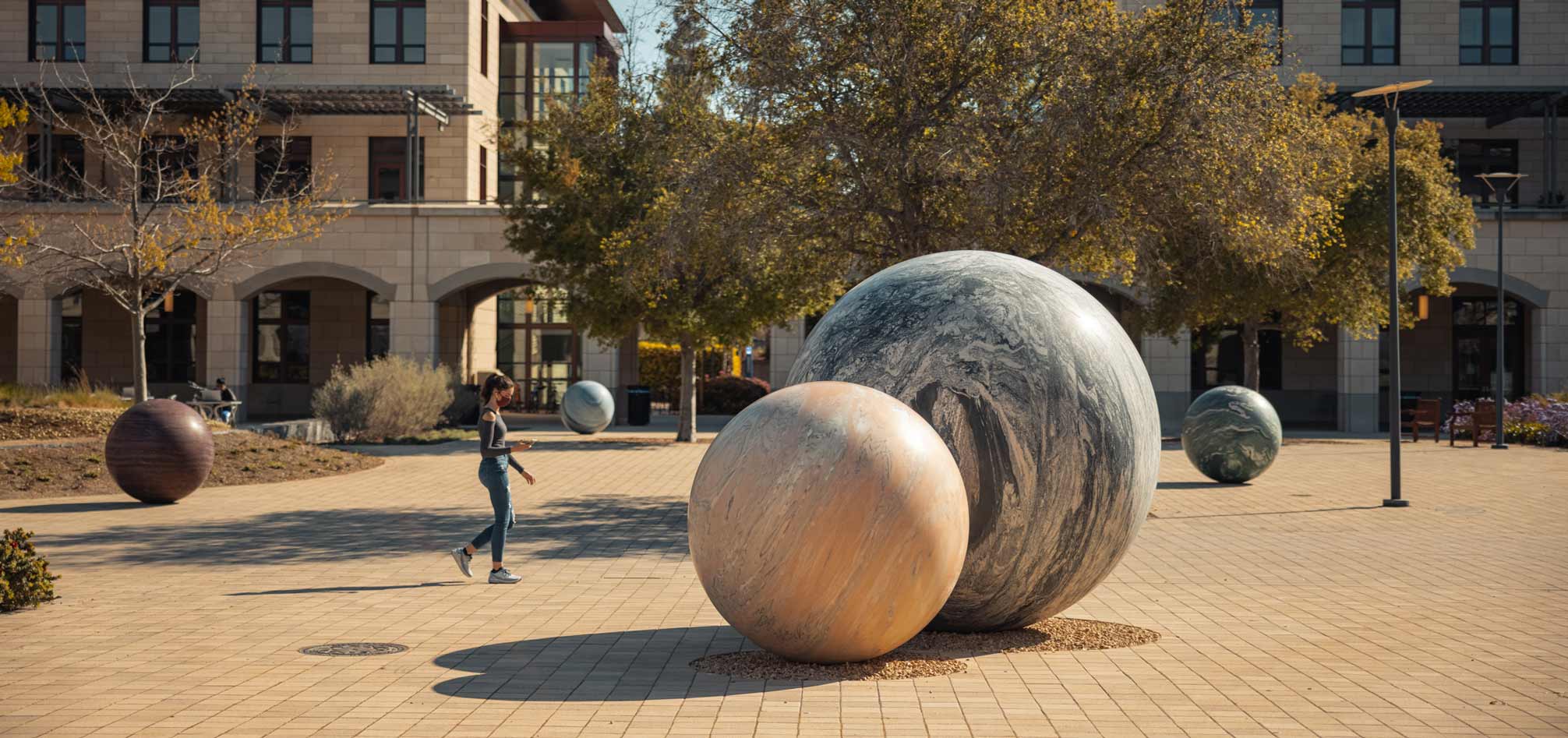 A young woman walks between some of the spheres that make up Pars Pro Toto in the Science and Engineering Quad