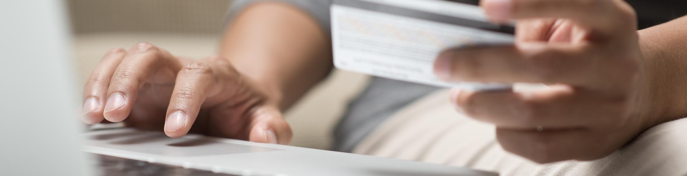 Photo of person holding a credit card while on a laptop.