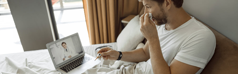 sick man lying in bed with a kleenex and a thermometer