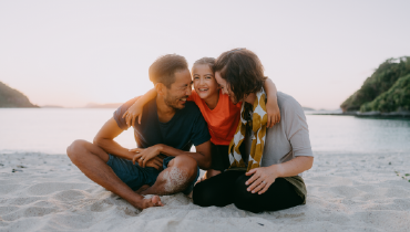 A mother, father, and child play on a beach together.