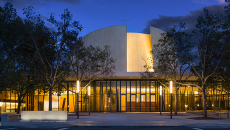 Bing Concert Hall at night, with light glowing through glass walls.