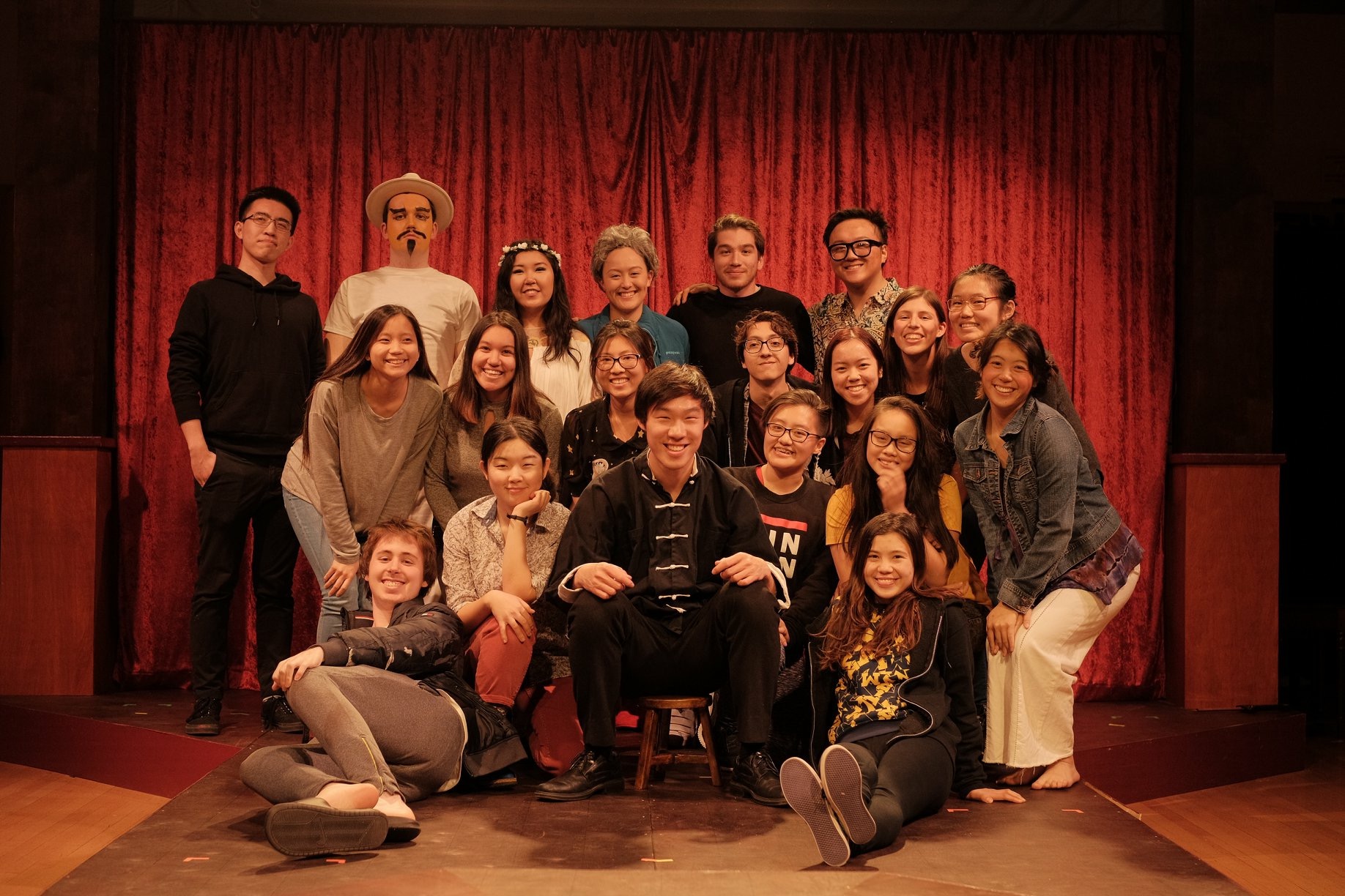 A group of cast members in front of a stage curtain.