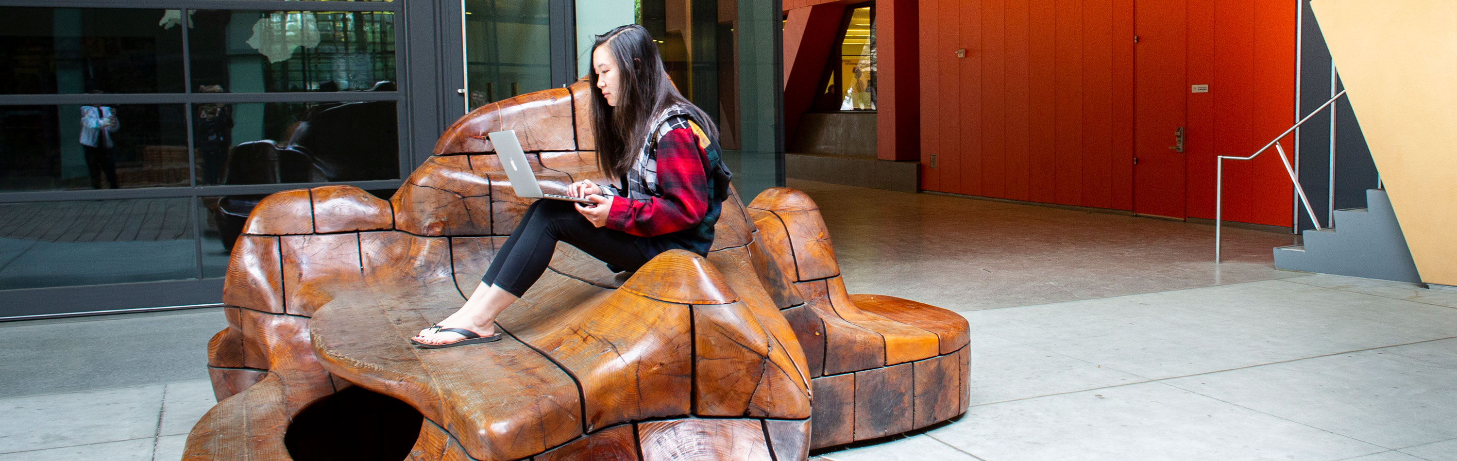 Student sitting on outside sculpture looking at her laptop computer