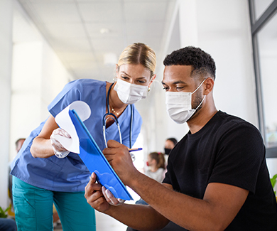 A masked medical attendant helps a patient fill in a survey